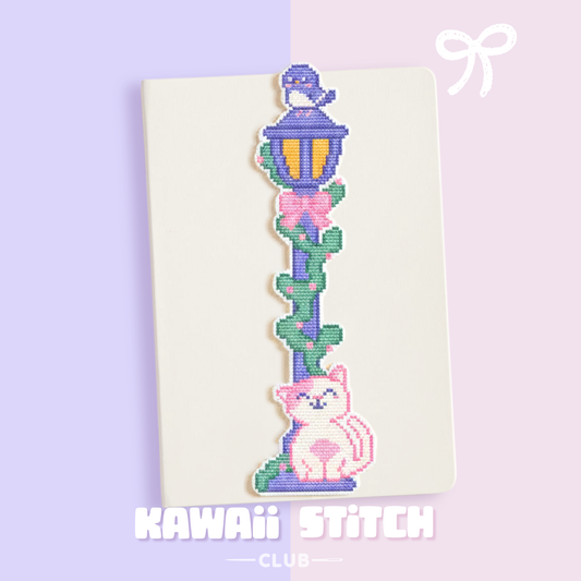 Pastel street lamp and cat cross stitch bookmark placed on an open book