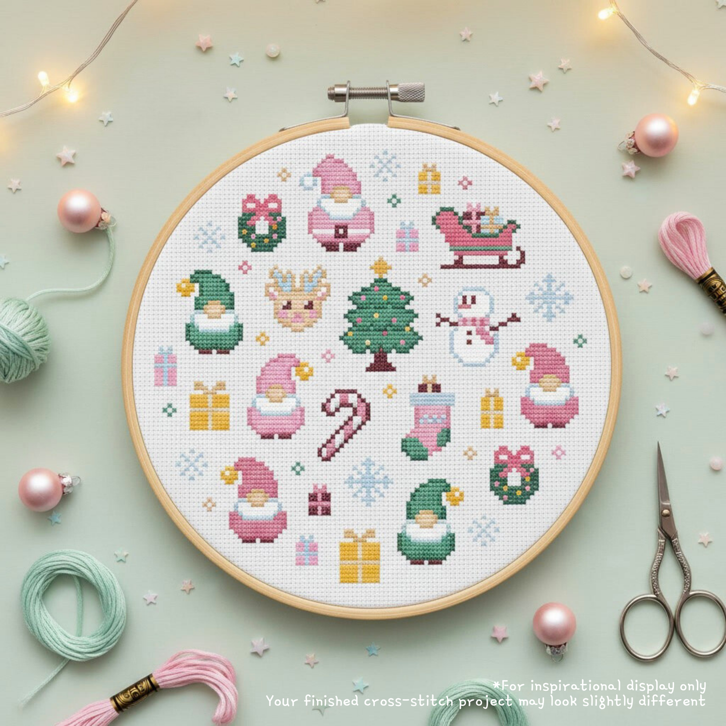 Pink Santa cross stitch displayed in a hoop with pink and mint floss, scissors, ornaments and fairy lights