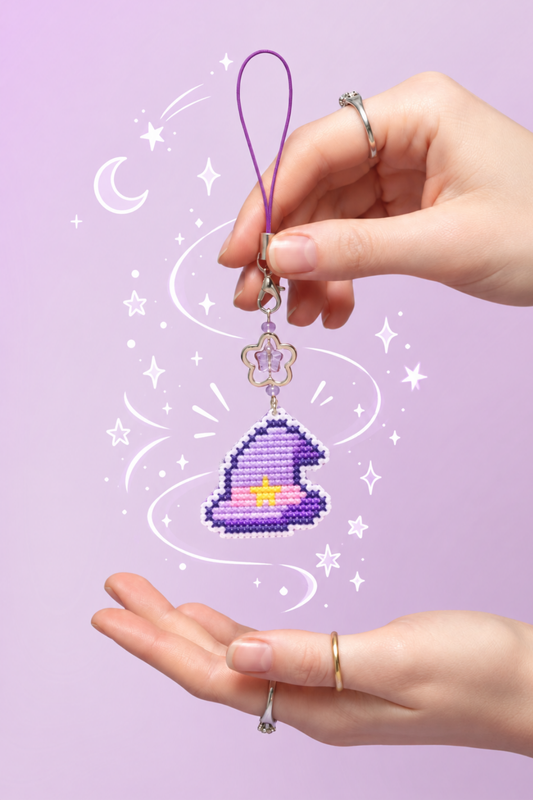 Pastel purple witch hat cross stitch keychain held by hand on a soft lavender magical background
