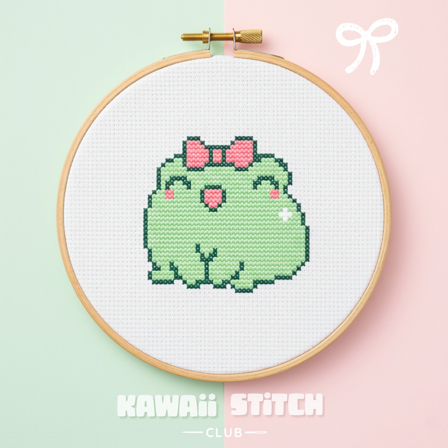 Green frog with a pink bow cross stitch design displayed in a wooden embroidery hoop