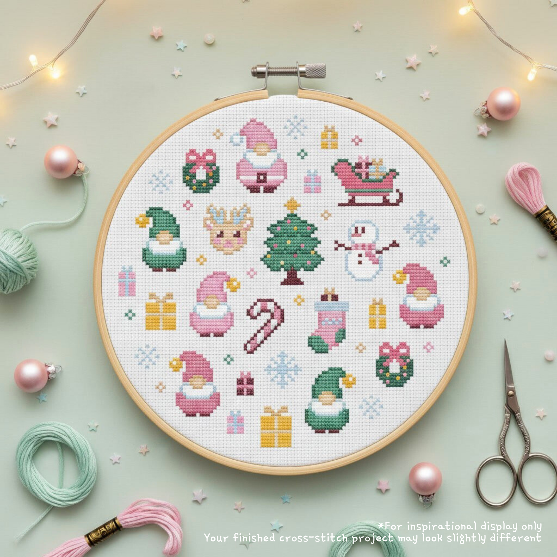 Pink Santa cross stitch displayed in a hoop with pink and mint floss, scissors, ornaments and fairy lights