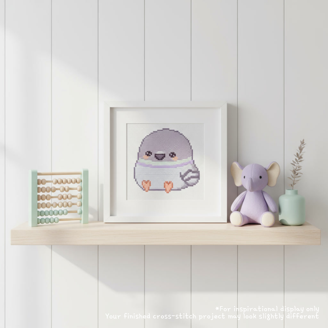 Framed pastel baby pigeon cross stitch displayed on a nursery shelf